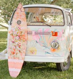 an old vw bus with flowers painted on the side and a surfboard leaning against it