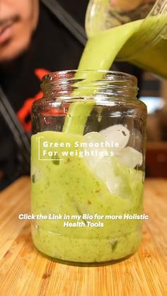 a person pouring green smoothie into a jar