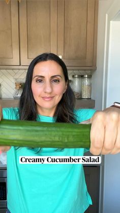 a woman is holding a cucumber in her hands with the words creamy cucumber salad on it