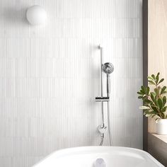 a white bath tub sitting next to a plant in a bathroom under a shower faucet