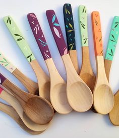 six wooden spoons lined up next to each other on a white surface with leaves painted on them