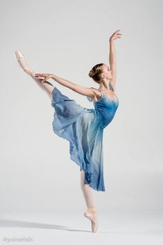 a ballerina in a blue dress is doing a ballet move with her arms stretched out
