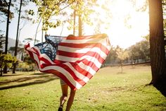 a woman is holding an american flag in the park with sun shining through her hair