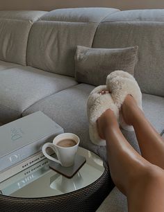 a person's feet resting on a couch next to a coffee cup and books
