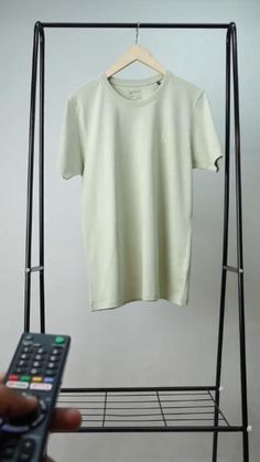 a person holding a remote control in front of a t - shirt hanging on a clothes rack
