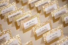 place cards are lined up on a table with gold glittered paper and white envelopes