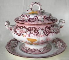 a pink and white tea pot on a saucer with an ornate design around the lid