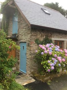 an old stone house with blue doors and flowers in the foreground on a rainy day