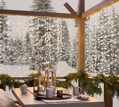 a dining room table set for christmas dinner with lights hanging from the ceiling and snow covered trees in the background