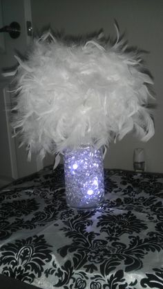a vase filled with white feathers sitting on top of a black and white table cloth