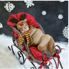 a baby is laying in a sleigh with a reindeer hat and scarf on