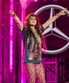 a woman standing on top of a stage with her arms in the air and wearing leggings