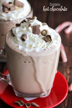 two hot chocolate drinks with whipped cream and candy canes on the side, sitting on a red saucer