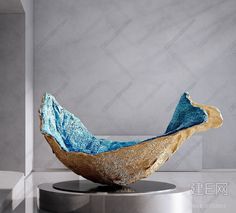 a blue and gold sculpture sitting on top of a metal stand in front of a gray wall
