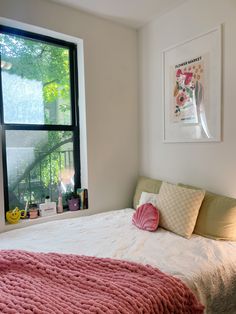 a bedroom with a pink blanket on the bed and pictures hanging over the window sill
