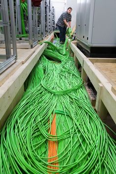 two men working in a factory with many green wires on the floor and one man standing next to it