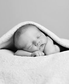 a black and white photo of a sleeping baby wrapped in a blanket with his eyes closed