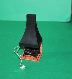 a miniature black fireplace on a green surface with a white cord attached to the chimney