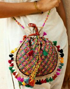 a woman wearing a white dress and holding a colorful purse with tassels on it