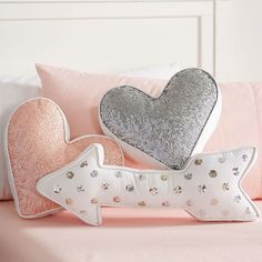 two heart shaped pillows sitting on top of a pink bed next to a white headboard