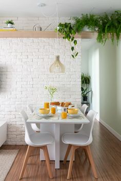 a dining room table with white chairs and plates on it, next to a brick wall