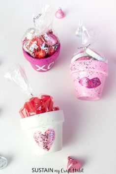 three heart shaped candies in pink containers on a white surface with candy hearts scattered around them