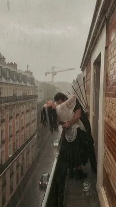 a man and woman kissing on top of a building in the rain with buildings behind them