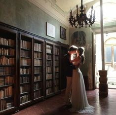 a bride and groom standing in front of bookshelves with their arms around each other
