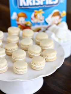 a white plate topped with mini macaroons next to a box of rice krispies