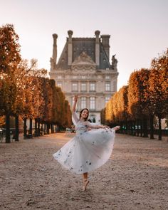 a woman is dancing in front of an old building with trees on the ground and leaves all around her