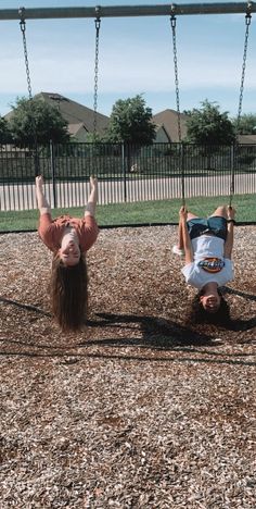 two children playing on a swing set in a park with their hands up to the ground