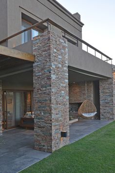 an outside view of a modern home with stone columns and patio furniture on the lawn