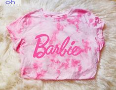 a pink tie dye shirt with the word barbie written on it, sitting on a fluffy white rug