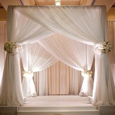 a decorated stage with white drapes and flowers