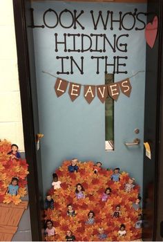 a door decorated with fall leaves and the words look who's hiding in the leaves