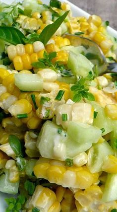 a white plate topped with corn and cucumber next to a green leafy garnish