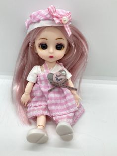 a doll with long pink hair wearing a dress and bow on it's head