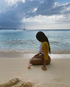 a woman sitting on top of a sandy beach next to the ocean under a cloudy sky