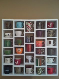 a white shelf filled with cups and mugs on top of each other next to a wall
