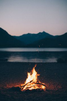a campfire is lit on the beach with mountains in the background
