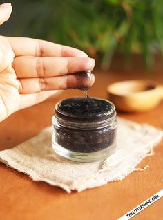 a hand holding a spoon over a jar of black stuff on top of a wooden table