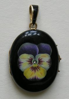 a black and yellow flower with purple centers on a gold chain hanging from a white wall