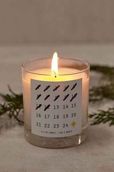 a candle with a calendar on it sitting next to evergreen branches and pine needles in the background