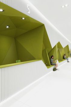 people are sitting on benches in a room with white walls and green geometric design,