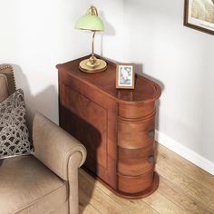 a small wooden cabinet next to a chair with a lamp on top of it in a living room