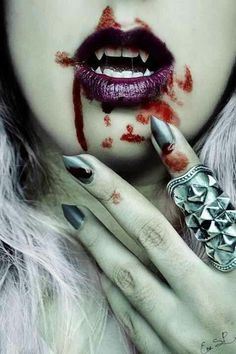 a woman's face with blood on her lips and nails, holding a ring