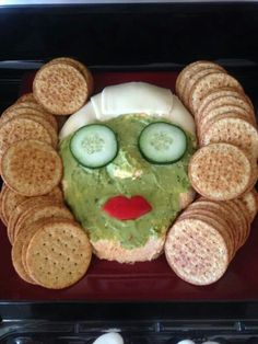 a face made out of crackers with cucumber slices around it and eyes