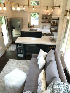 a living room and kitchen area in a tiny home with wood flooring, white walls, black cabinets, and gray couches