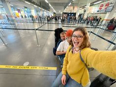 a woman taking a selfie with her friends at an airport baggage claim area while waiting for their flight
