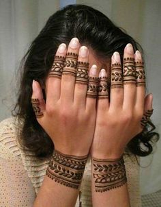 a woman holding her hands to her face with henna tattoos on it's arms